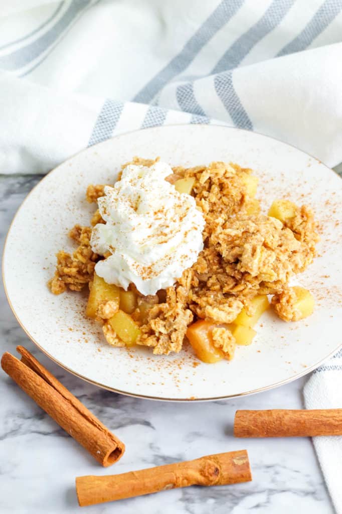 gluten free apple crisp served on a white plate topped with whipped cream