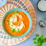 pumpkin and sweet potato soup, served in a blue bowl, topped with fresh herbs and coconut cream