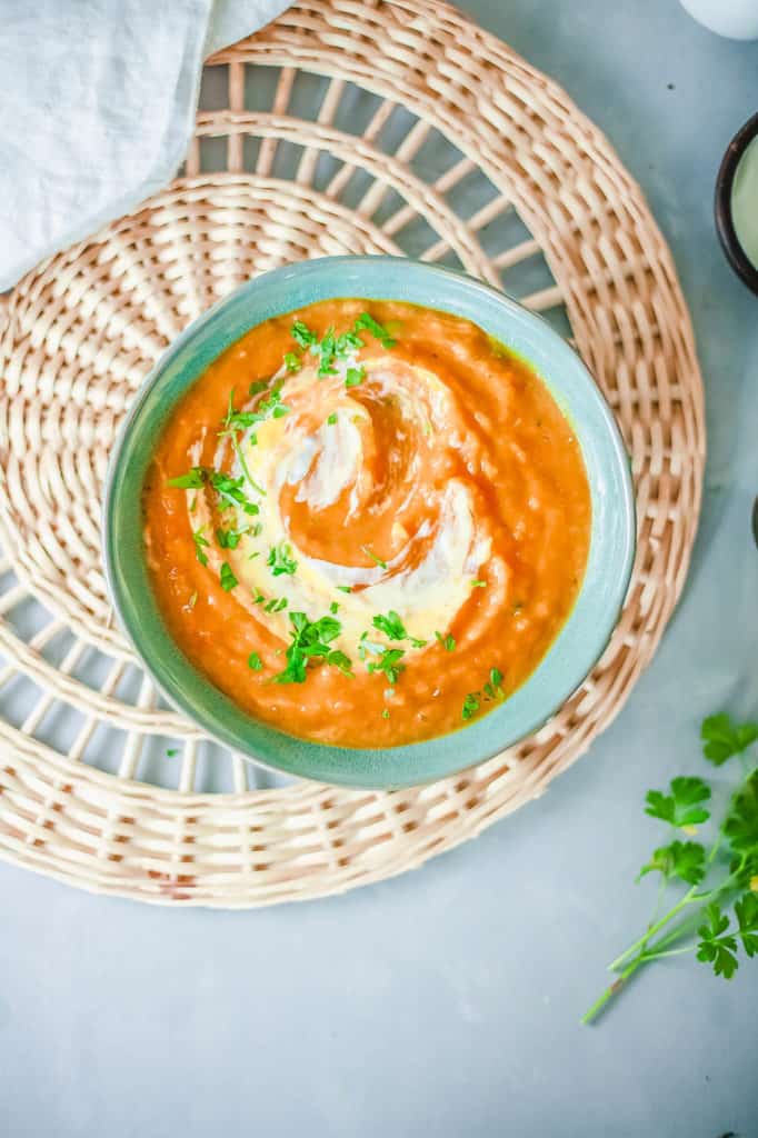 pumpkin and sweet potato soup, served in a blue bowl, topped with fresh herbs and coconut cream