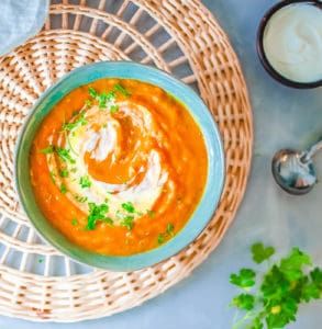 pumpkin and sweet potato soup, served in a blue bowl, topped with fresh herbs and coconut cream