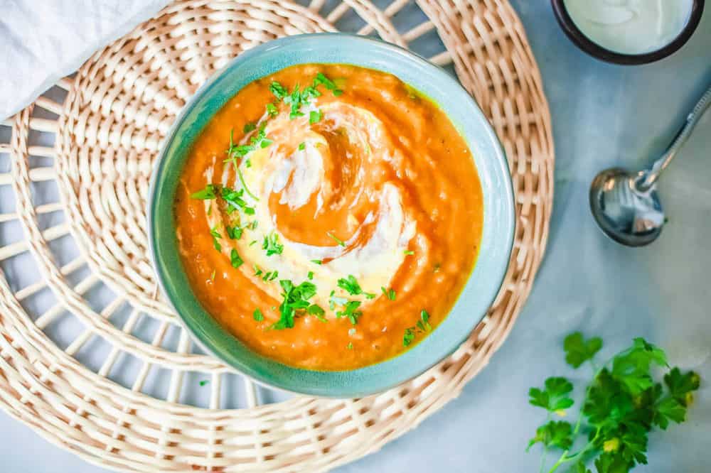 pumpkin and sweet potato soup, served in a blue bowl, topped with fresh herbs and coconut cream