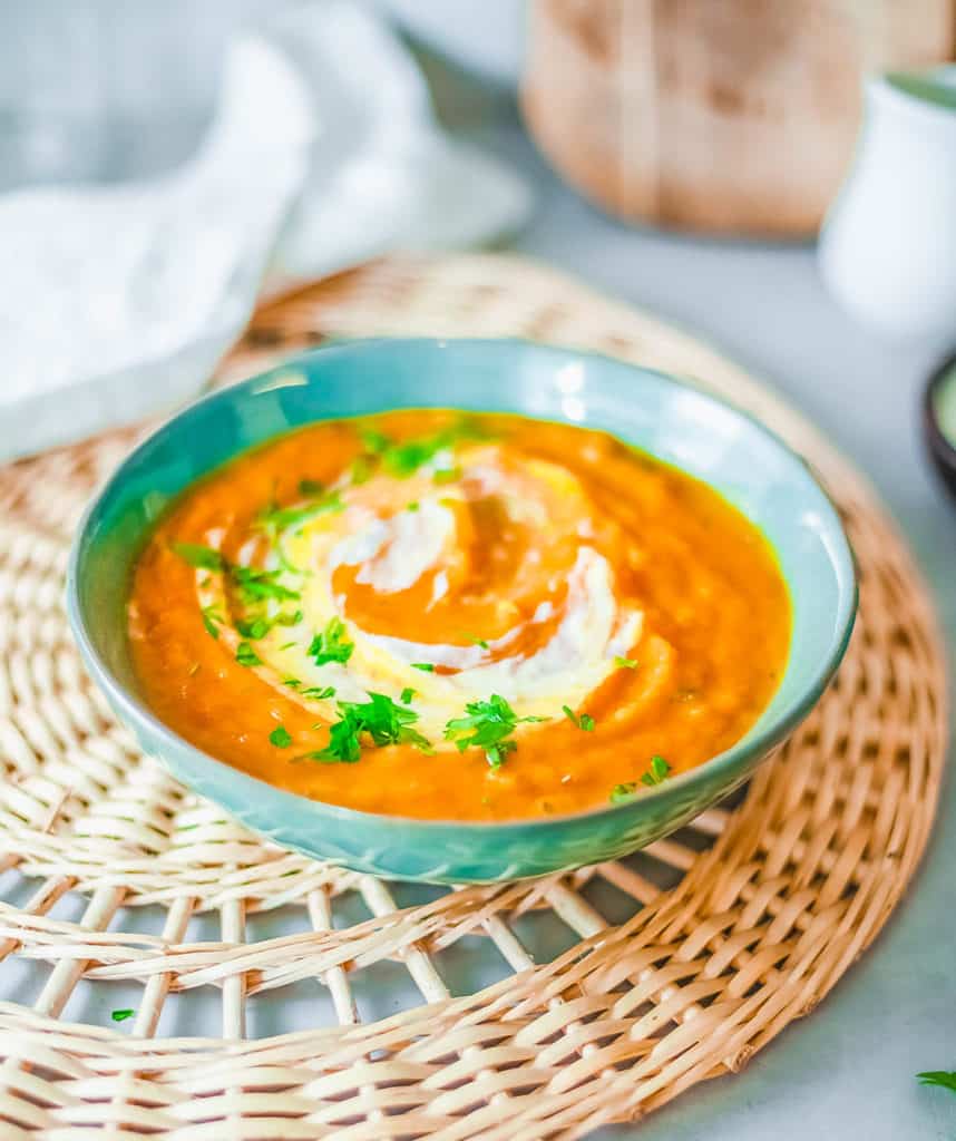 pumpkin and sweet potato soup, served in a blue bowl, topped with fresh herbs and coconut cream