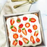 three milk cake topped with whipped cream frosting and strawberries in a square pan