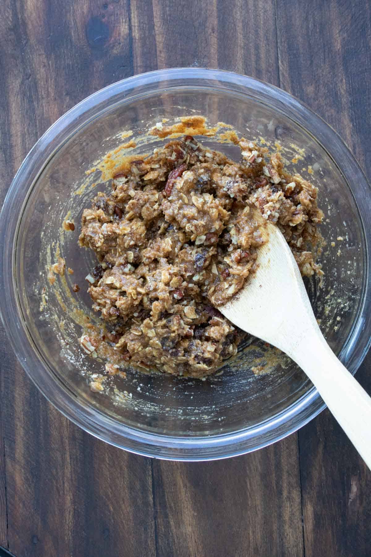 Vegan oatmeal raisin cookie dough in a clear glass bowl with wooden spoon.