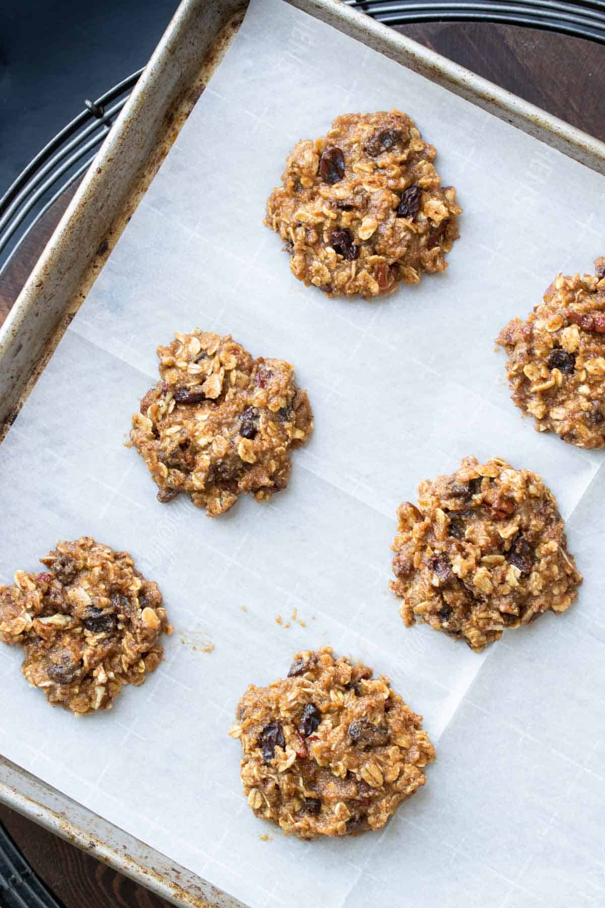 Unbaked vegan gf oatmeal raisin cookies spread out on a baking sheet.