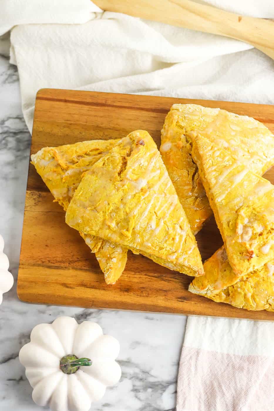 vegan healthy pumpkin scones with pumpkin on a cutting board, drizzled with a maple glaze