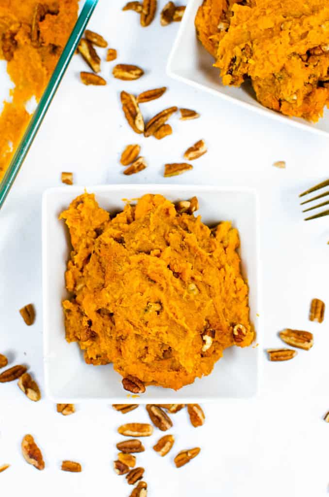 one scoop of vegan sweet potato casserole served in a white bowl with pecans sprinkled on top