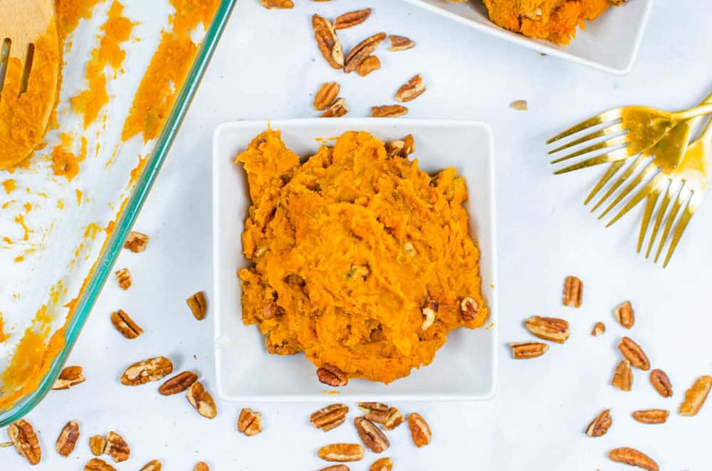 one scoop of vegan sweet potato casserole served in a white bowl with pecans sprinkled on top