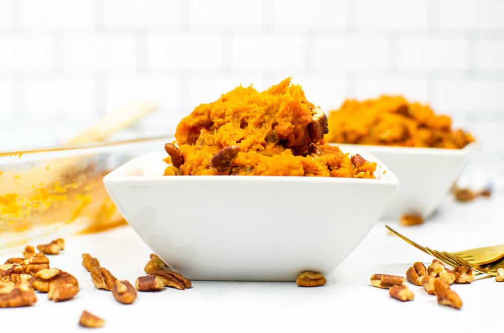 one scoop of vegan sweet potato casserole served in a white bowl with pecans sprinkled on top