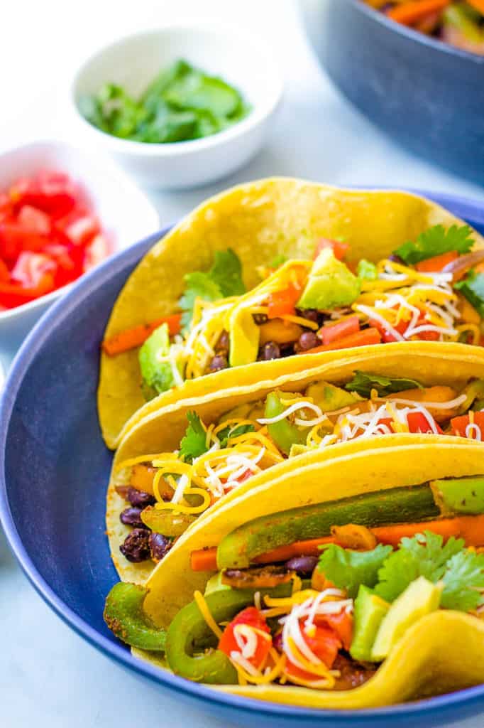 vegetarian fajitas in a corn tortilla topped with cheese, avocado and cilantro, served in a blue bowl