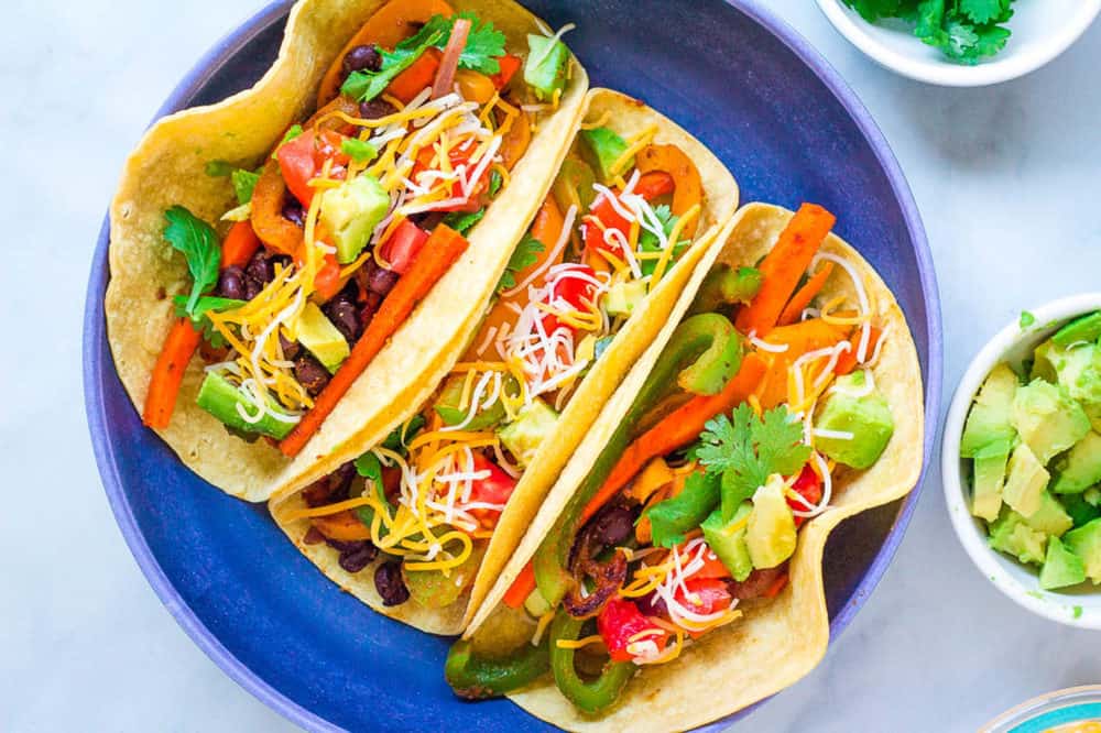 top view of vegetarian fajitas in a corn tortilla topped with cheese, avocado and cilantro, served in a blue bowl