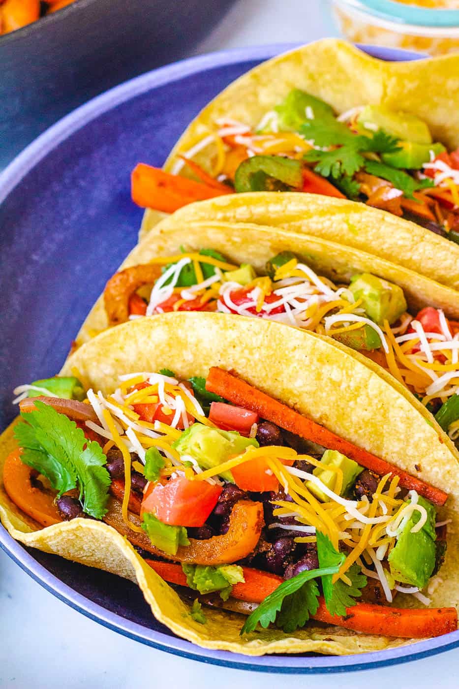 vegetarian fajitas in a corn tortilla topped with cheese, avocado and cilantro, served in a blue bowl