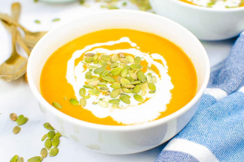 finished soup in a white bowl topped with pumpkin seeds and coconut cream