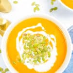 carrot ginger soup in a white bowl topped with pumpkin seeds and coconut cream