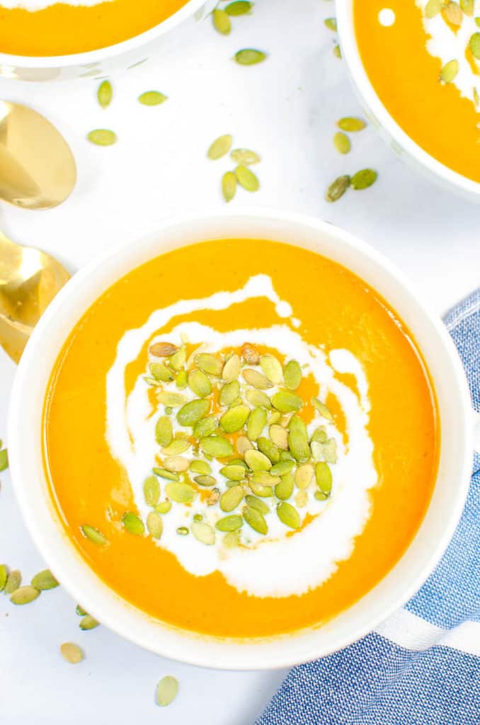 carrot ginger soup in a white bowl topped with pumpkin seeds and coconut cream