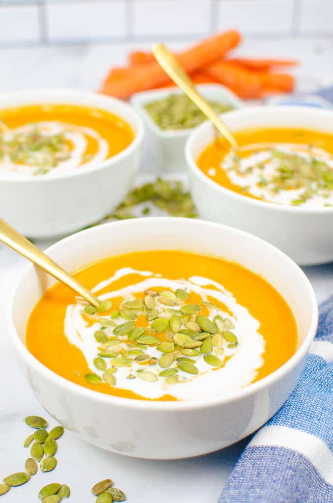 carrot ginger soup in a white bowl topped with pumpkin seeds and coconut cream