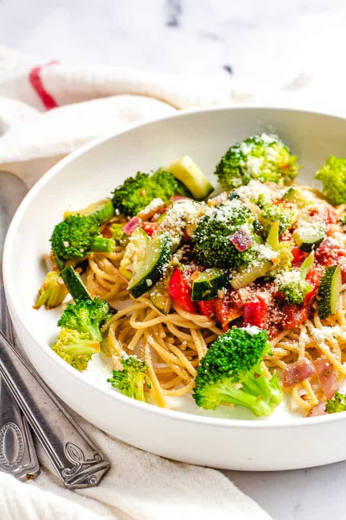 garlic pasta with veggies in a white bowl with parmesan cheese
