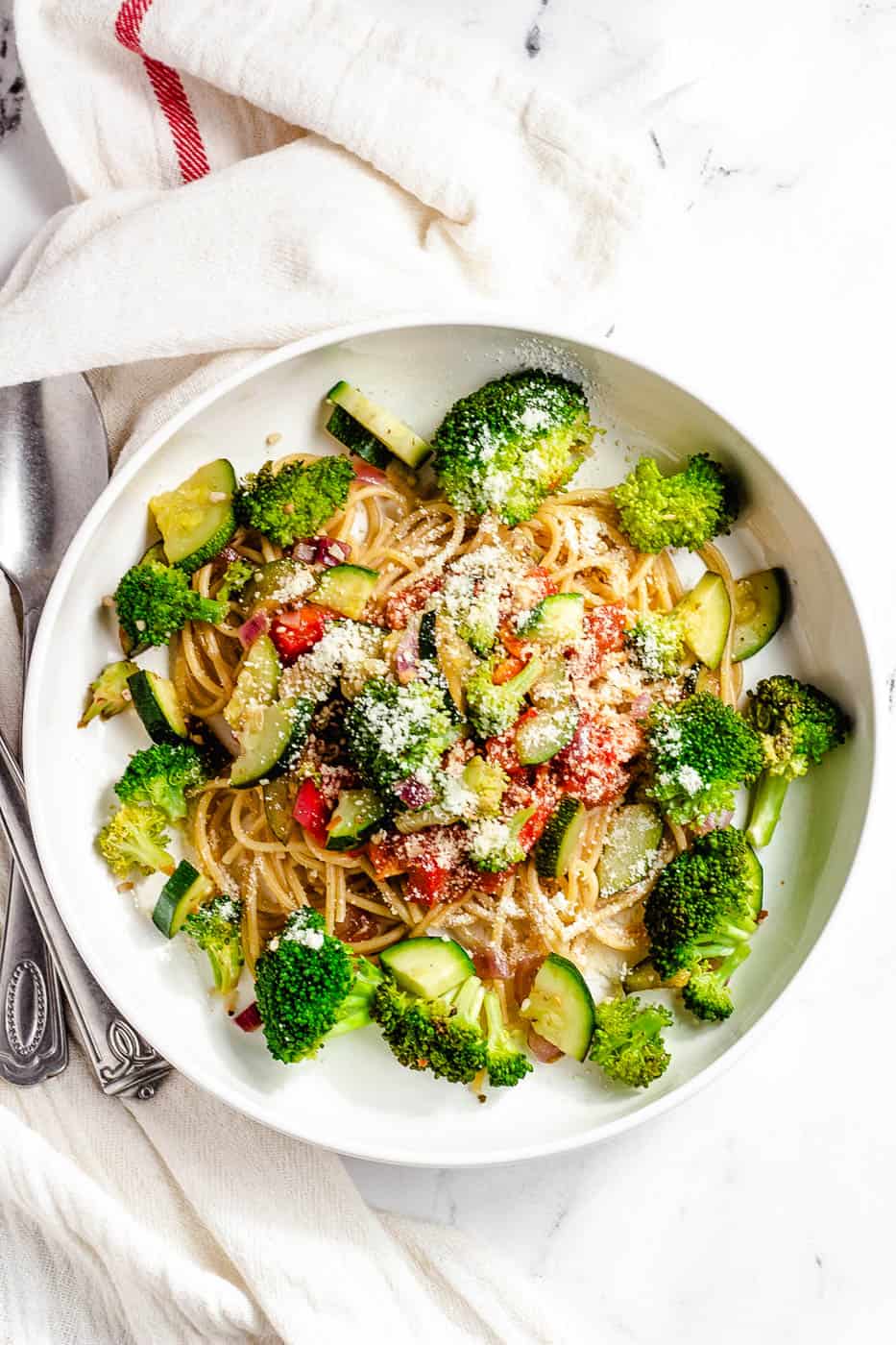 garlic pasta with veggies in a white bowl with parmesan cheese