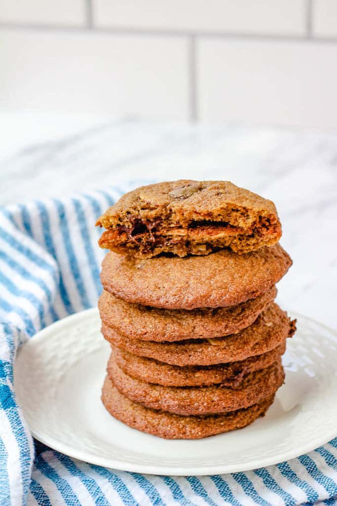 healthy chocolate chip cookies stacked on a cutting board, with one cookie broken for a closeup inside