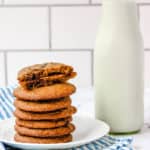 healthy chocolate chip cookies stacked on a cutting board, with one cookie broken for a closeup inside and milk in the background