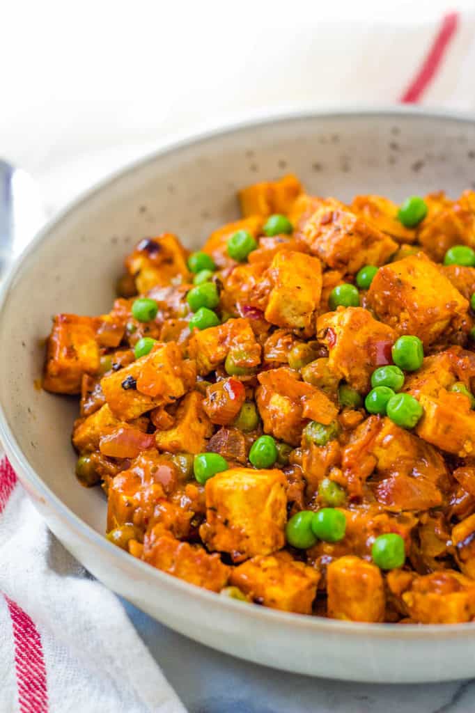 tofu paneer, mattar paneer in a white dish with peas and curry sauce