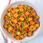 tofu paneer, mattar paneer in a white dish with peas and curry sauce
