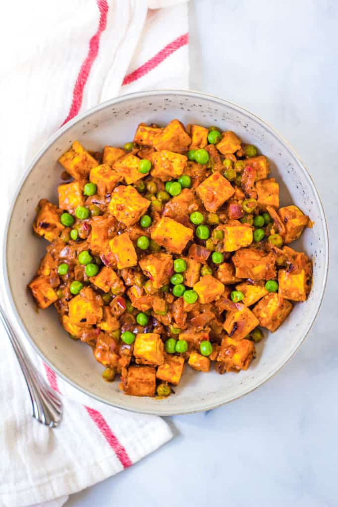 tofu paneer, mattar paneer in a white dish with peas and curry sauce