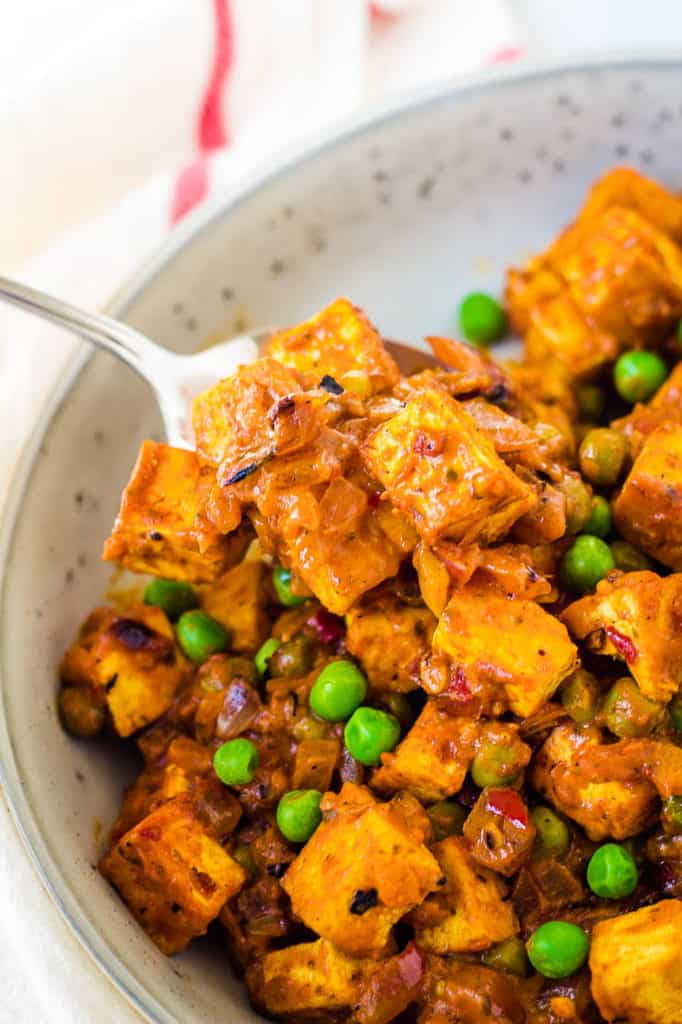 tofu paneer, mattar paneer in a white dish with peas and curry sauce