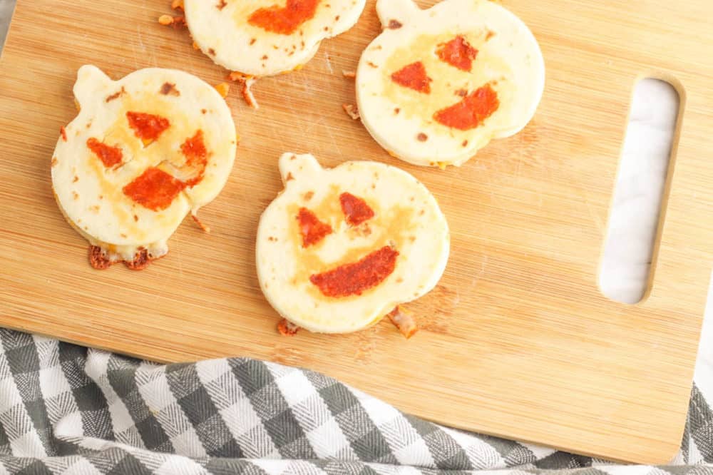 halloween jack-o-lantern pumpkin quesadillas served on a wooden cutting board