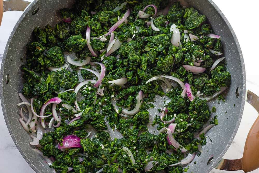 spinach added to onions in a pan.