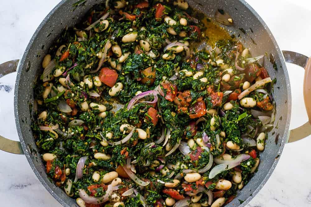 tomatoes and white beans added to spinach and onions in a pan