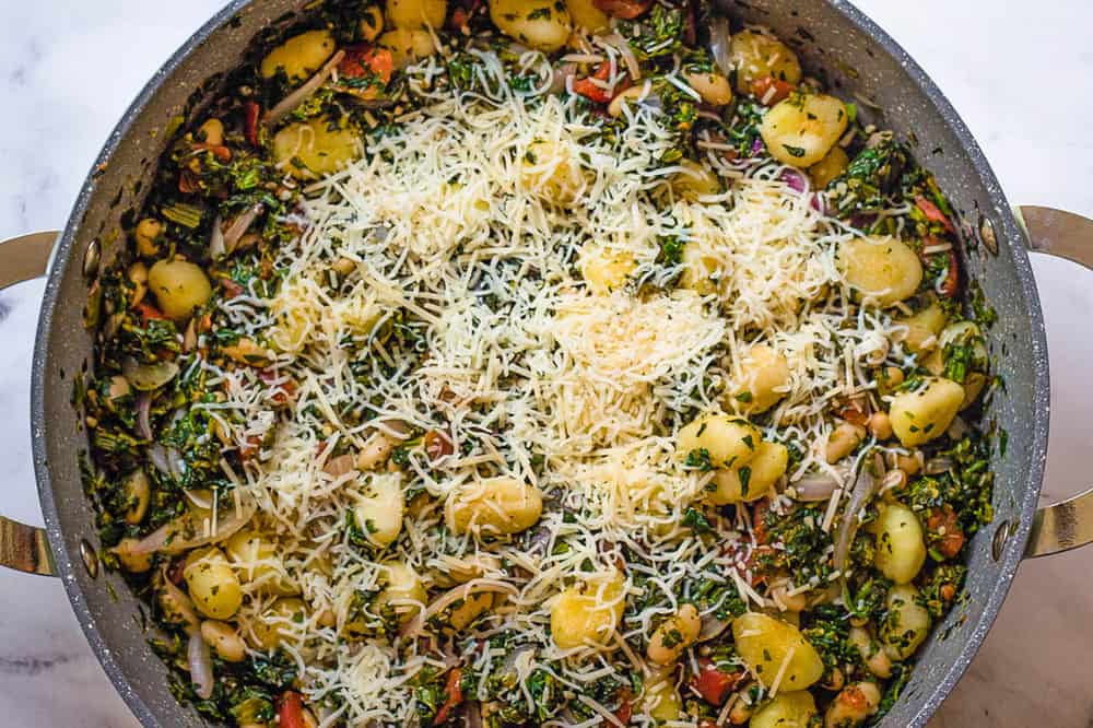 shredded cheese added to gnocchi in a pan.