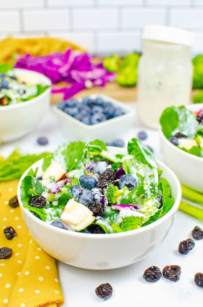 superfood salad served in a white bowl with broccoli, blueberries, sweet Fuji apples, cabbage, spinach, dried cherries, pine nuts, and a healthy ranch dressing
