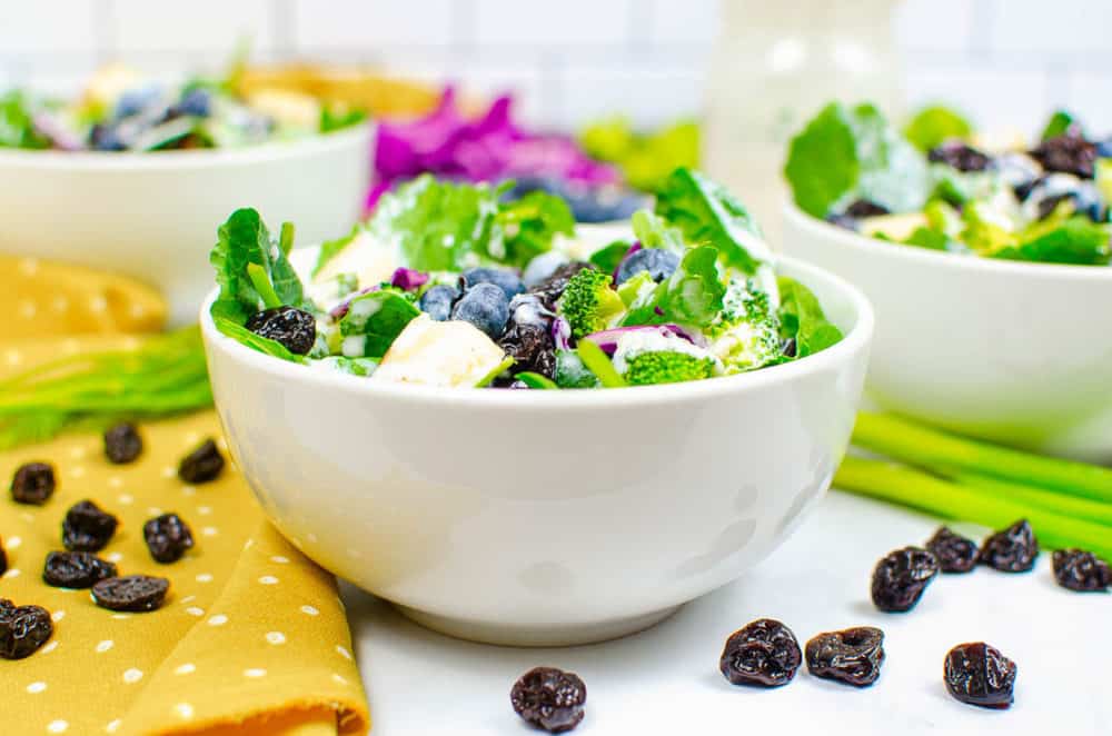 superfood salad served in a white bowl with broccoli, blueberries, sweet Fuji apples, cabbage, spinach, dried cherries, pine nuts, and a healthy ranch dressing
