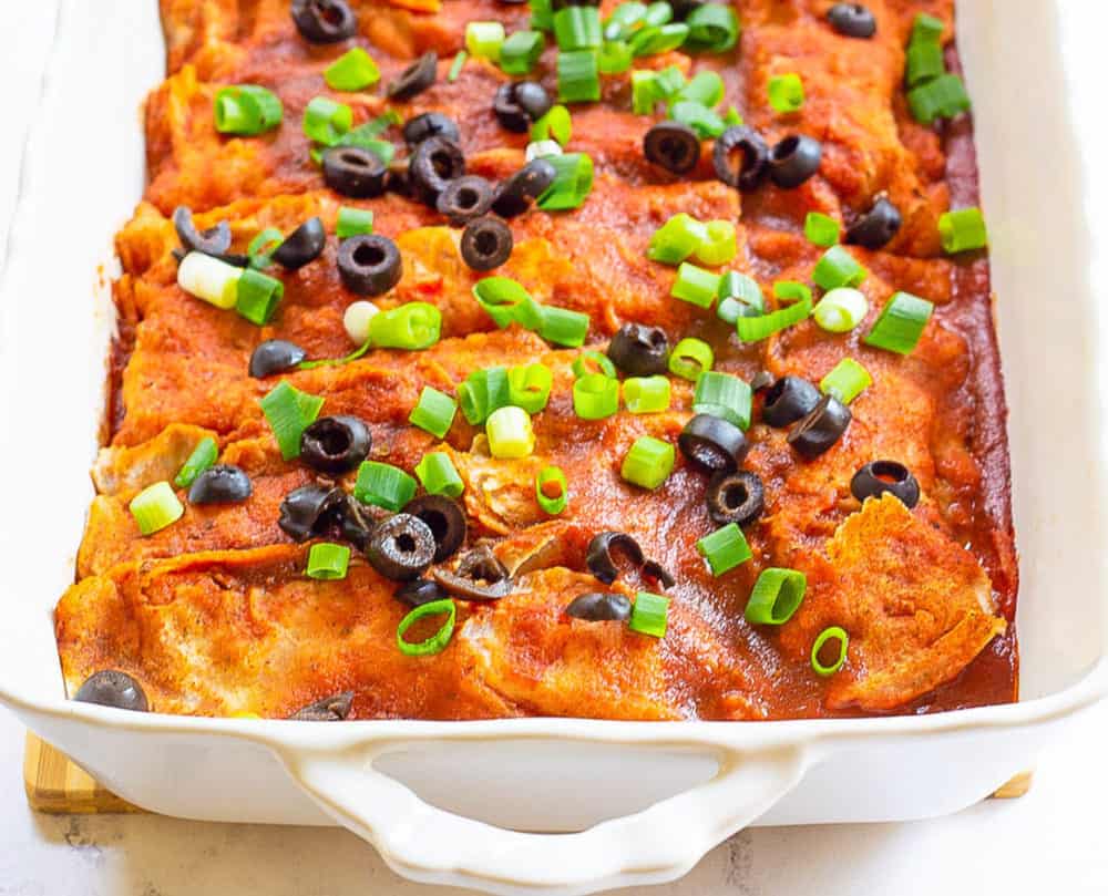 vegan enchiladas, fresh out of the oven, served in a casserole dish and topped with green onions and olives