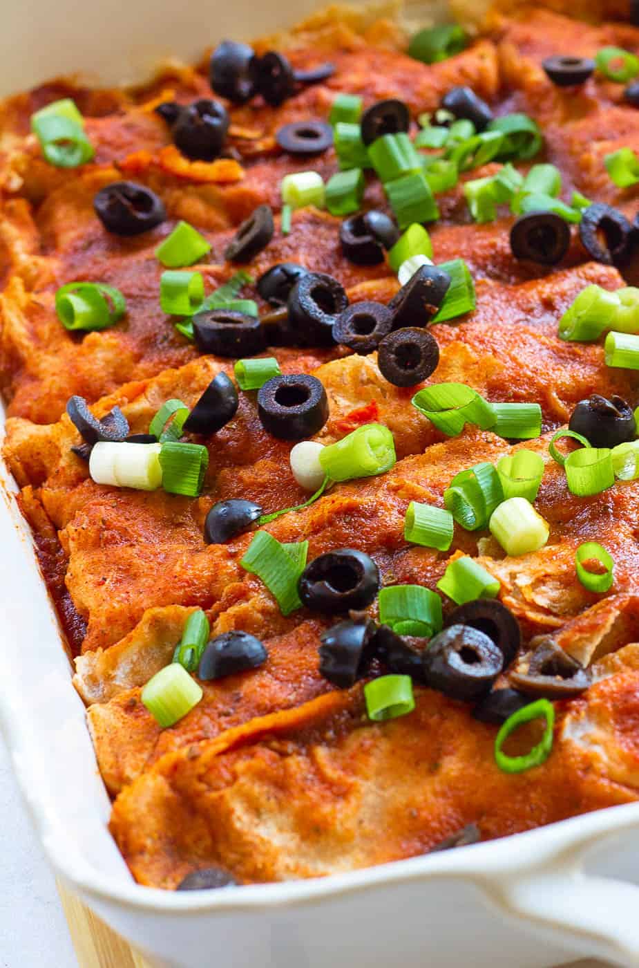 vegan enchiladas, fresh out of the oven, served in a casserole dish and topped with green onions and olives