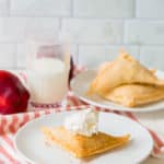 puff pastry apple turnovers topped with homemade whipped cream on a white plate