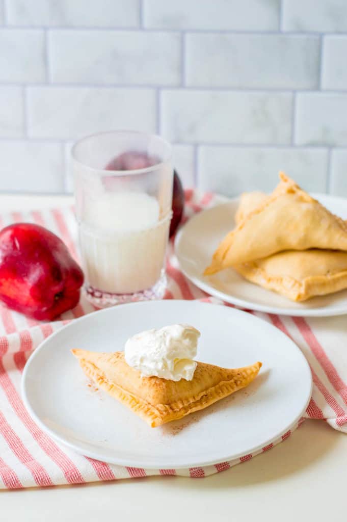 puff pastry apple turnovers topped with homemade whipped cream on a white plate