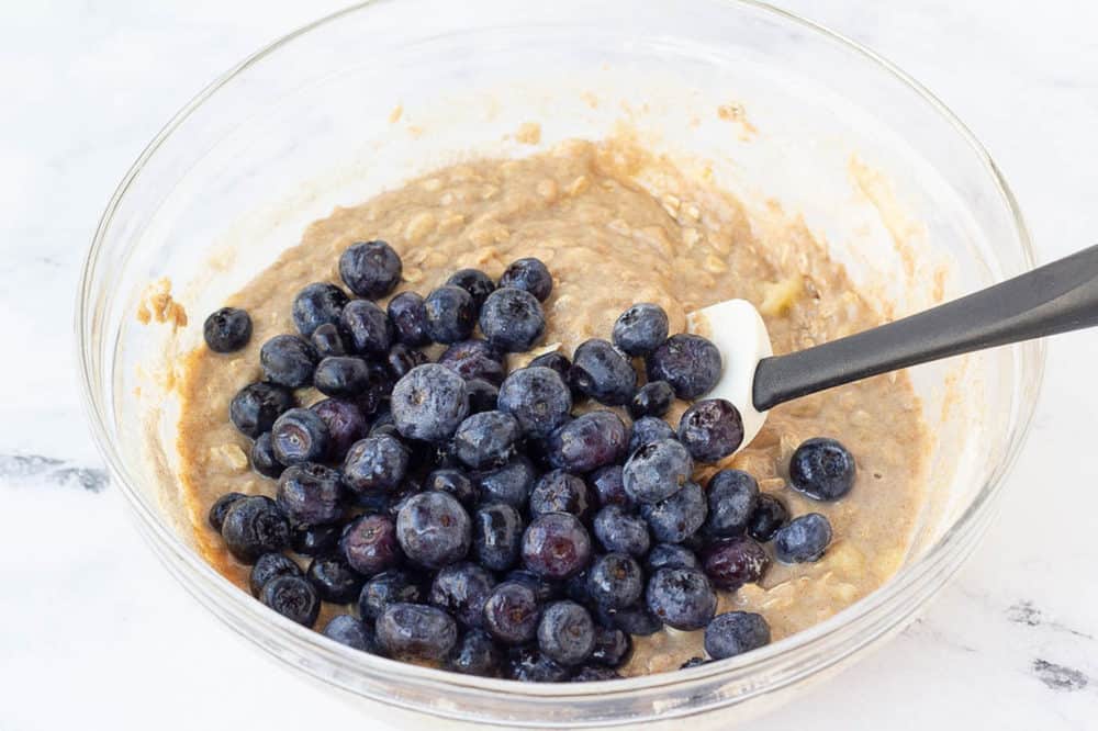 Fresh blueberries stirred into a bowl of bread batter.