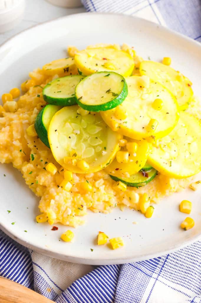 gluten free cheesy polenta topped with zucchini, corn and herbs, served on a white plate