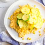 gluten free cheesy polenta topped with zucchini, corn and herbs, served on a white plate