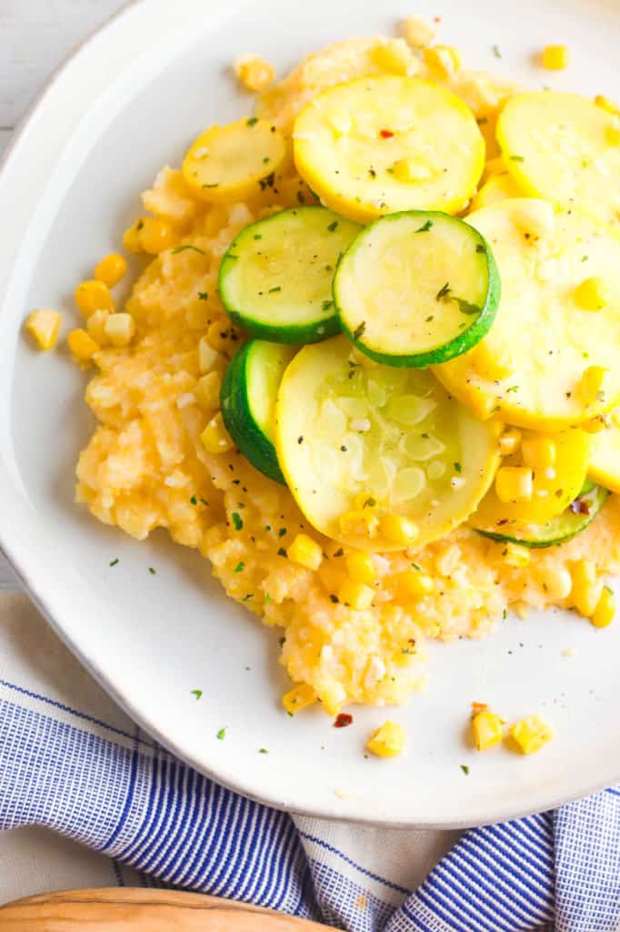 gluten free cheesy polenta topped with zucchini, corn and herbs, served on a white plate