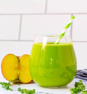 Healthy kale smoothie served in a glass with a straw and an apple on the side.