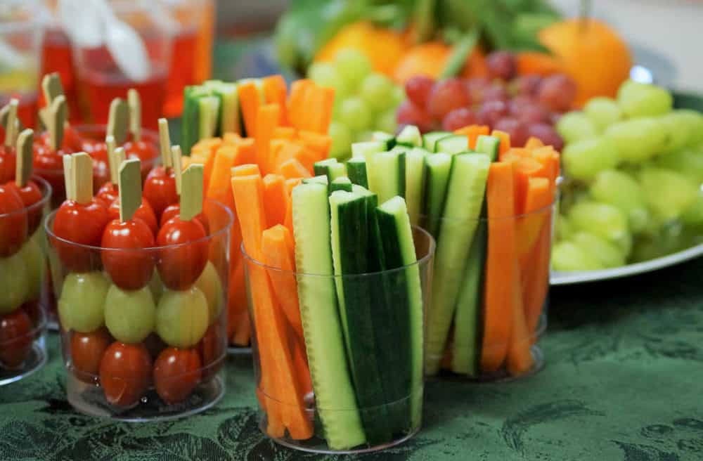 cucumber, carrot slices in small cups- plane Snacks of fresh fruits and vegetables including carrots, cucumbers, tomatoes and grapes on a table at a children’s party.