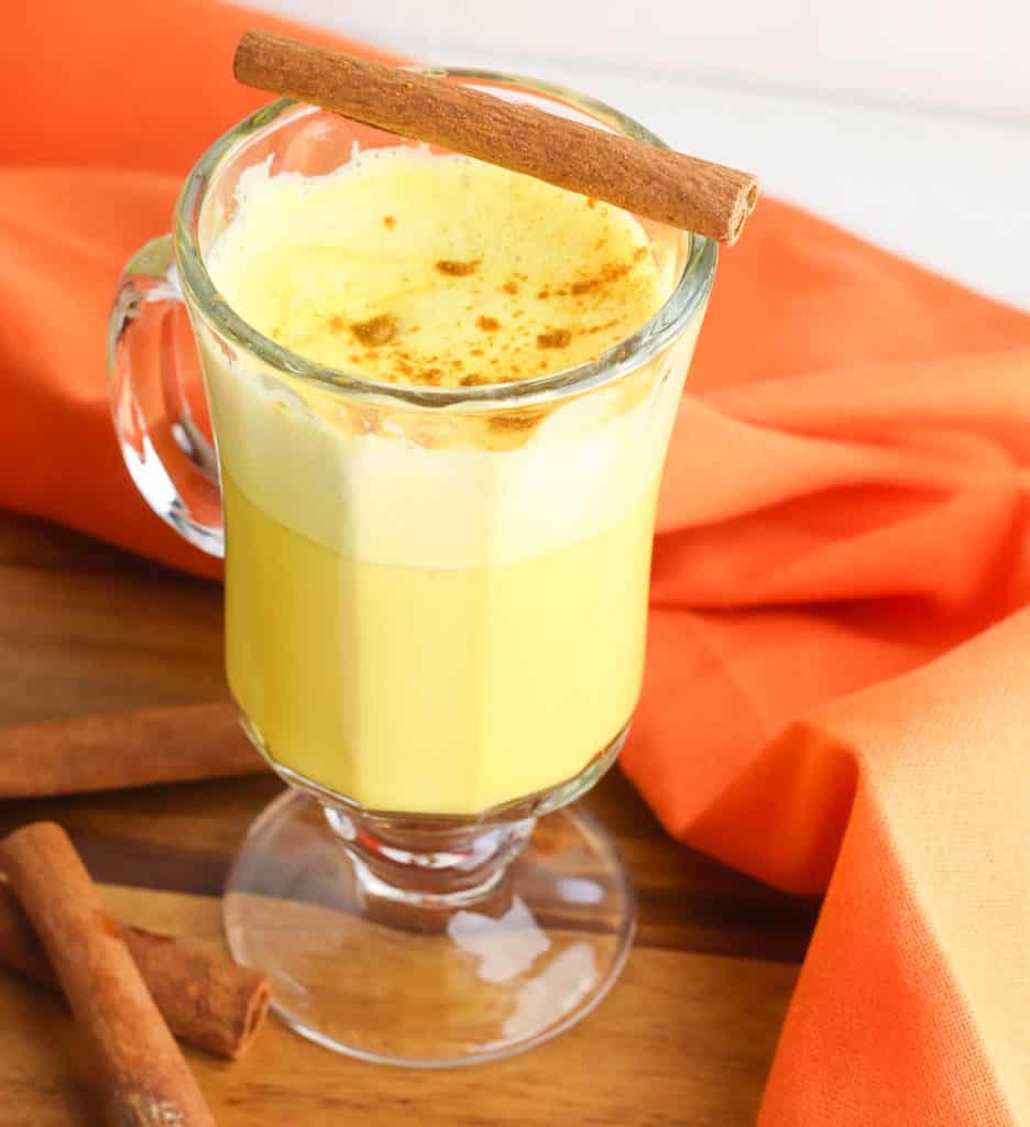 golden latte, golden milk latte (or turmeric latte) in a glass cup with cinnamon, against an orange background