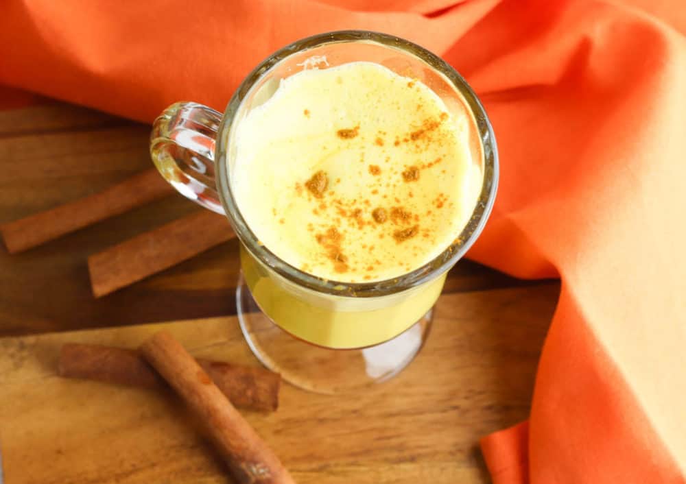 golden milk latte (or turmeric latte) in a glass cup with cinnamon, against an orange background