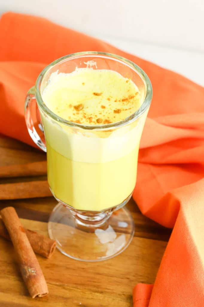 golden milk latte (or turmeric latte) in a glass cup with cinnamon, against an orange background