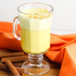 golden milk latte (or turmeric latte) in a glass cup with cinnamon, against an orange background