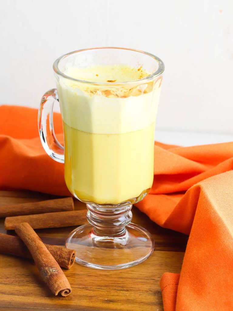 golden latte (or turmeric latte) in a glass cup with cinnamon, against an orange background