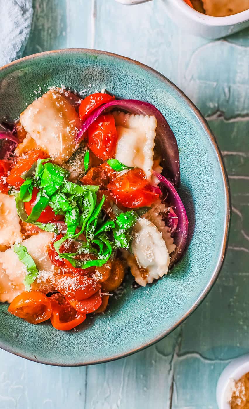 spinach ravioli with roasted tomatoes and basil in a blue bowl